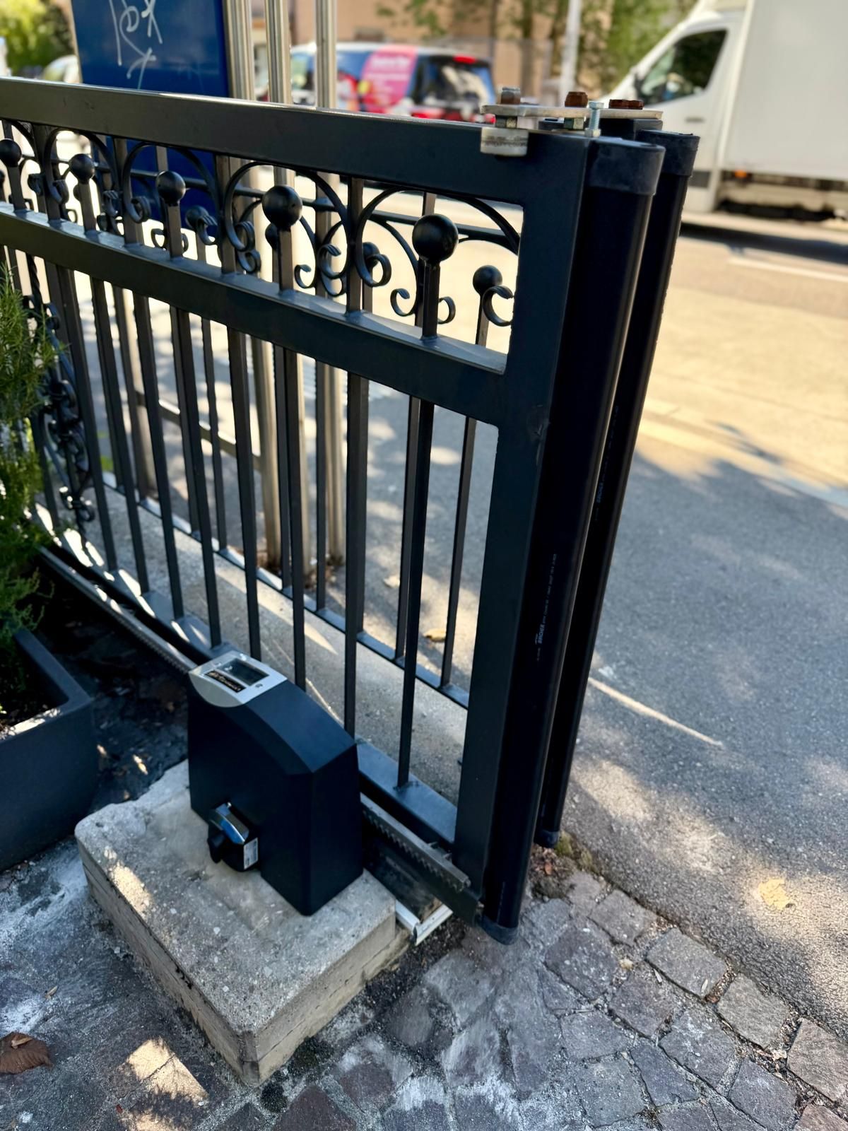 Schwarzes Schmiedeeisen-Schiebetor mit Antrieb auf einem Steinsockel