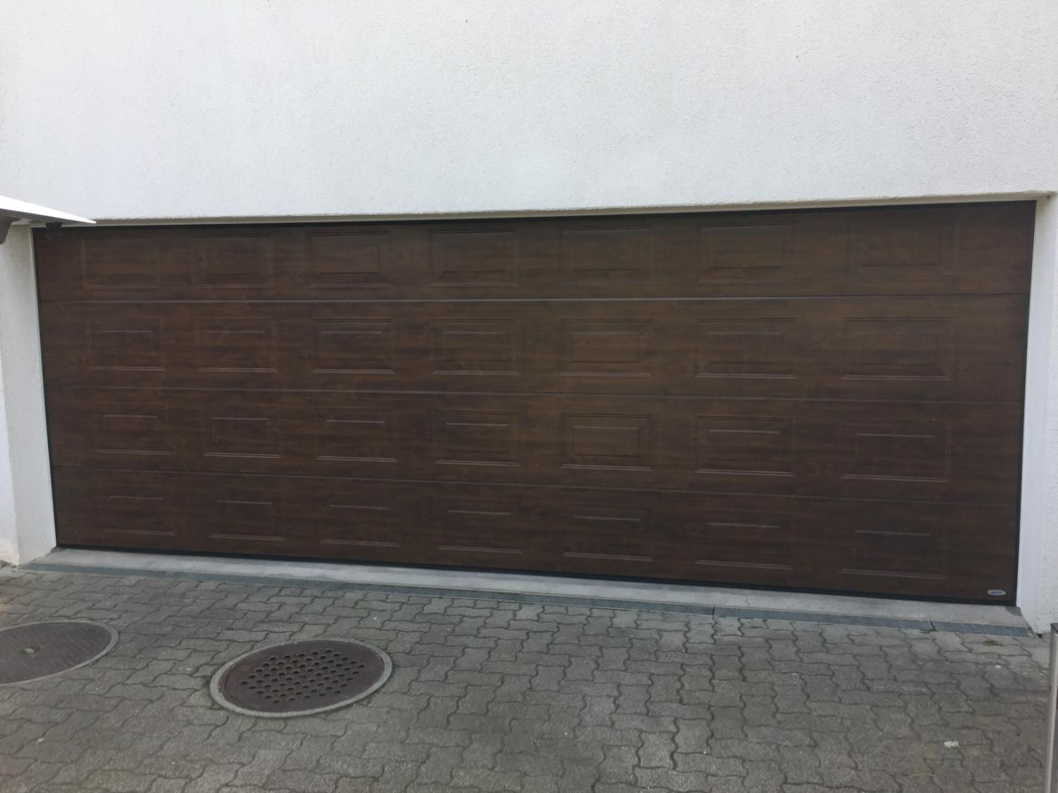 Sektionaltor in dunkler Holzoptik an einer weiss verputzten Garage